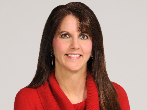 Picture of Lisa, a white woman with long Burnette hair, wearing a red sweater and silver earrings. She is in front of a neutral background.